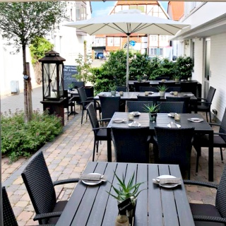 Außenansichten Gasthaus Clappertons Speisekammer Terrasse, schwarze Stühle und Tische, Sonnenschirm